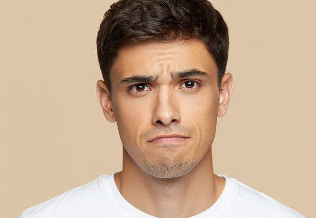 Молодой мужчина в белой футболке смотрит прямо в камеру с выражением лёгкого недоумения